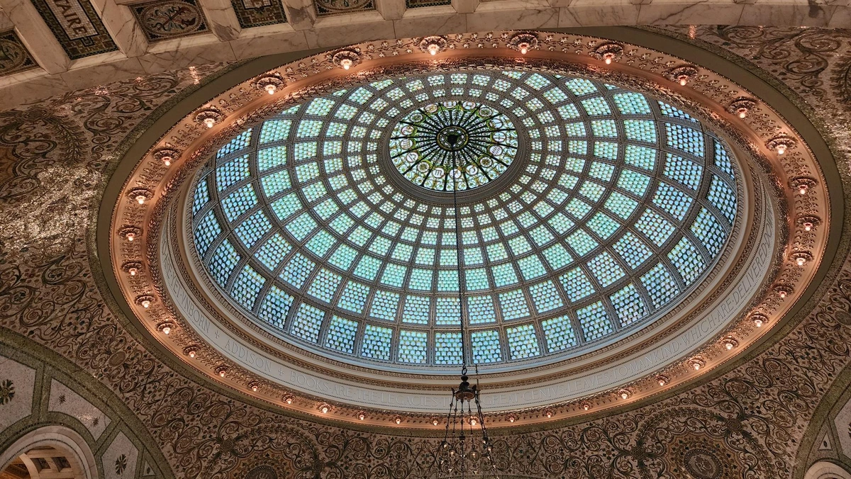 Oblique view of the large domed (from our perspective, oval) skylight, composed of thousands of light blue/white glass discs held together in metal frames that form a matrix around a central circle. In this circle are intricate floral and abstract designs and the 12 symbols of the zodiac.

Around the base of the dome is a ring of orange/white lights, and the surrounding ceiling is a mosaic of intricate floral designs on a white background.