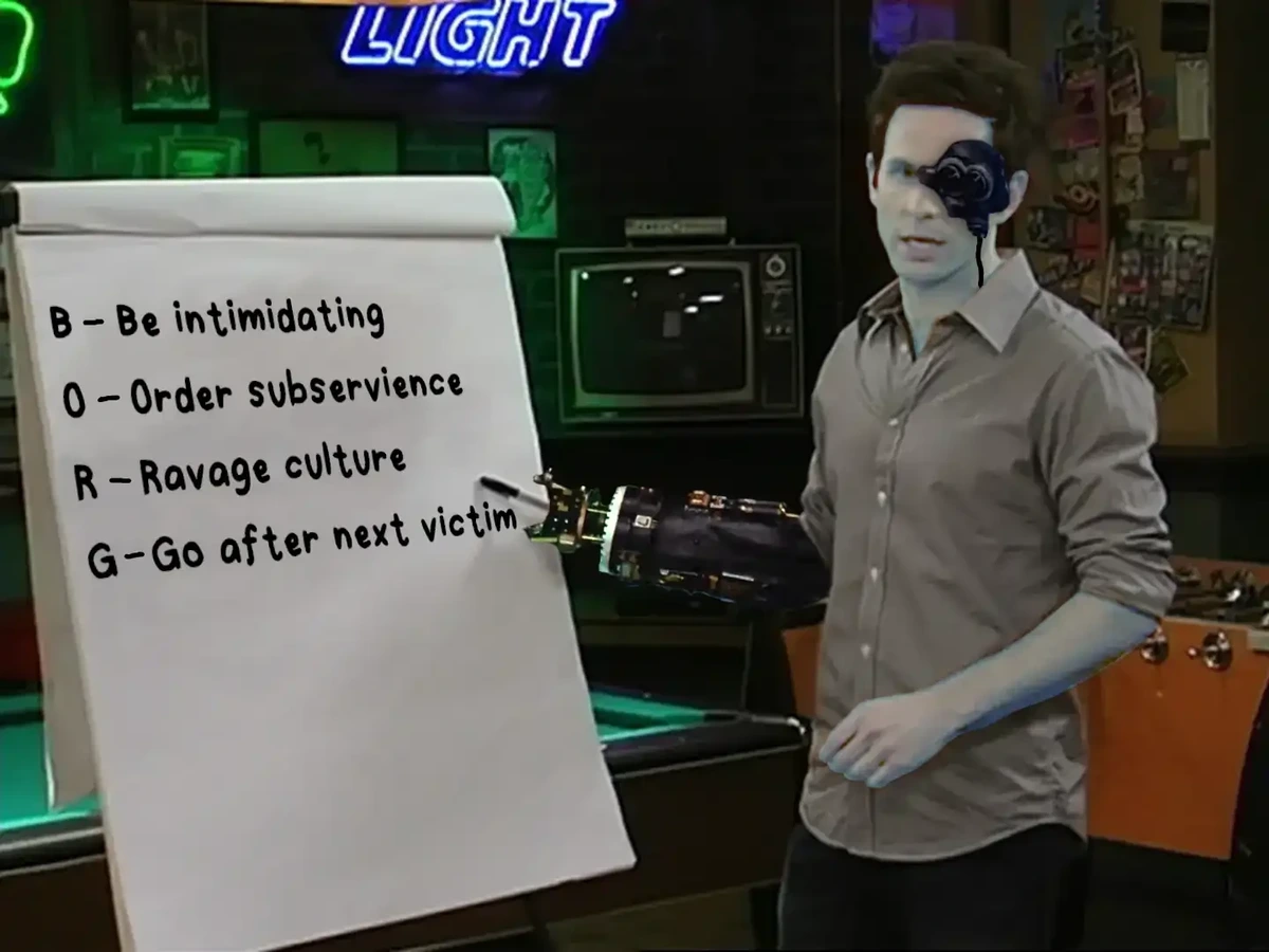 Dennis dressed as a Borg drone, complete with pale skin, ocular implant, and mechanical arm pointing at an easel that reads "B - Be intimidating, O - Order subservience, R - Ravage culture, G - Go after next victim"