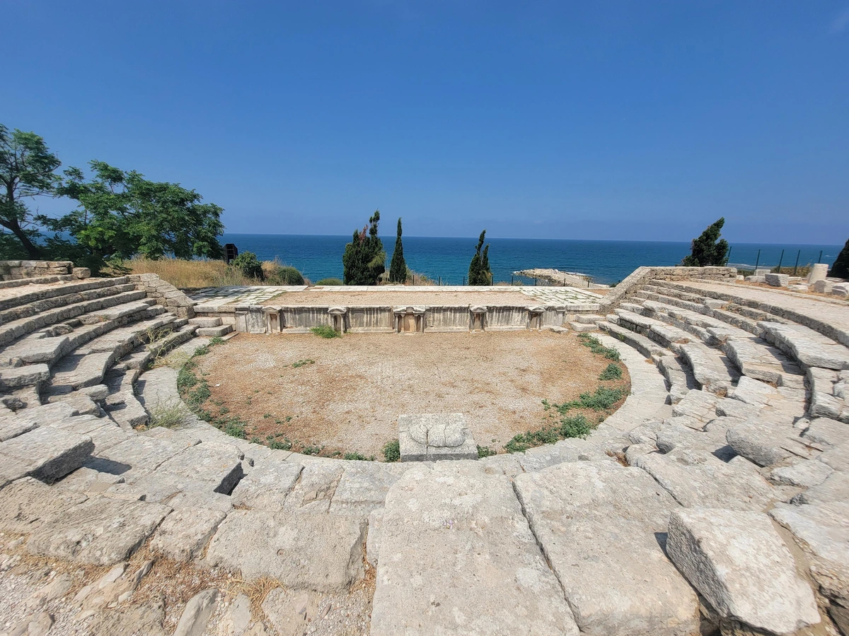 about 3/4 circle stone theater about 1.5 meters deep and 10 meters in diameter overlooking the mediterranean under a blue sky